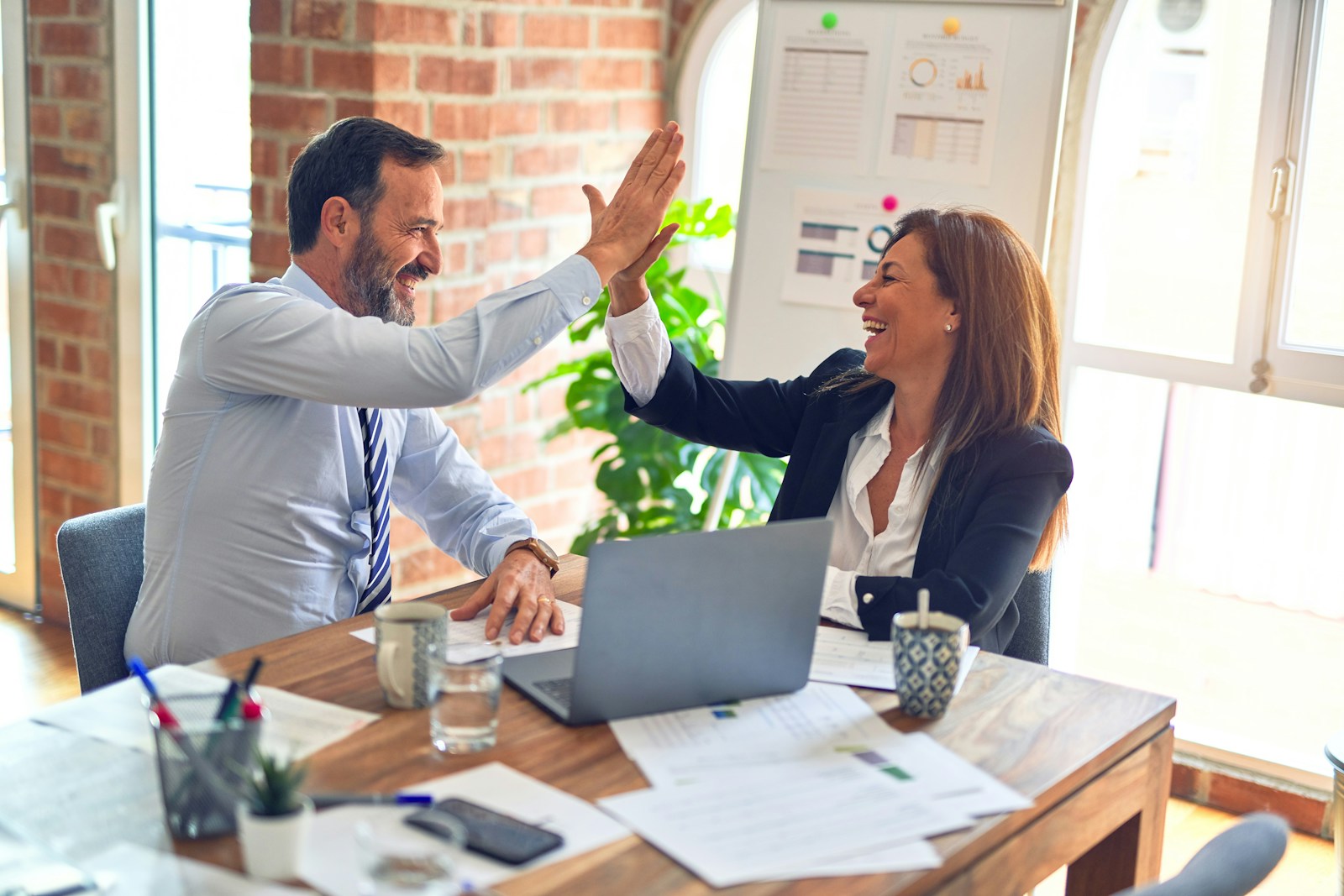Two colleagues shaking hands across a desk in a professional setting